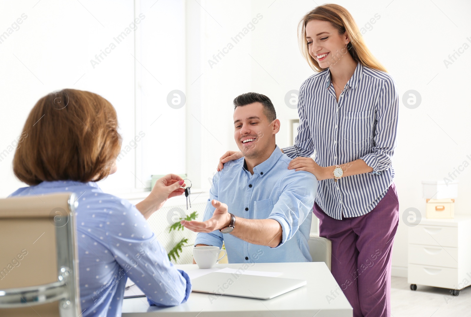 Photo of Real estate agent giving keys to young couple in office