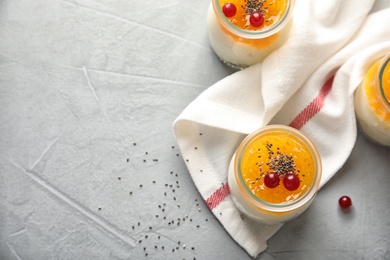 Photo of Creamy rice pudding with red currant and jam in jars on grey table, top view. Space for text