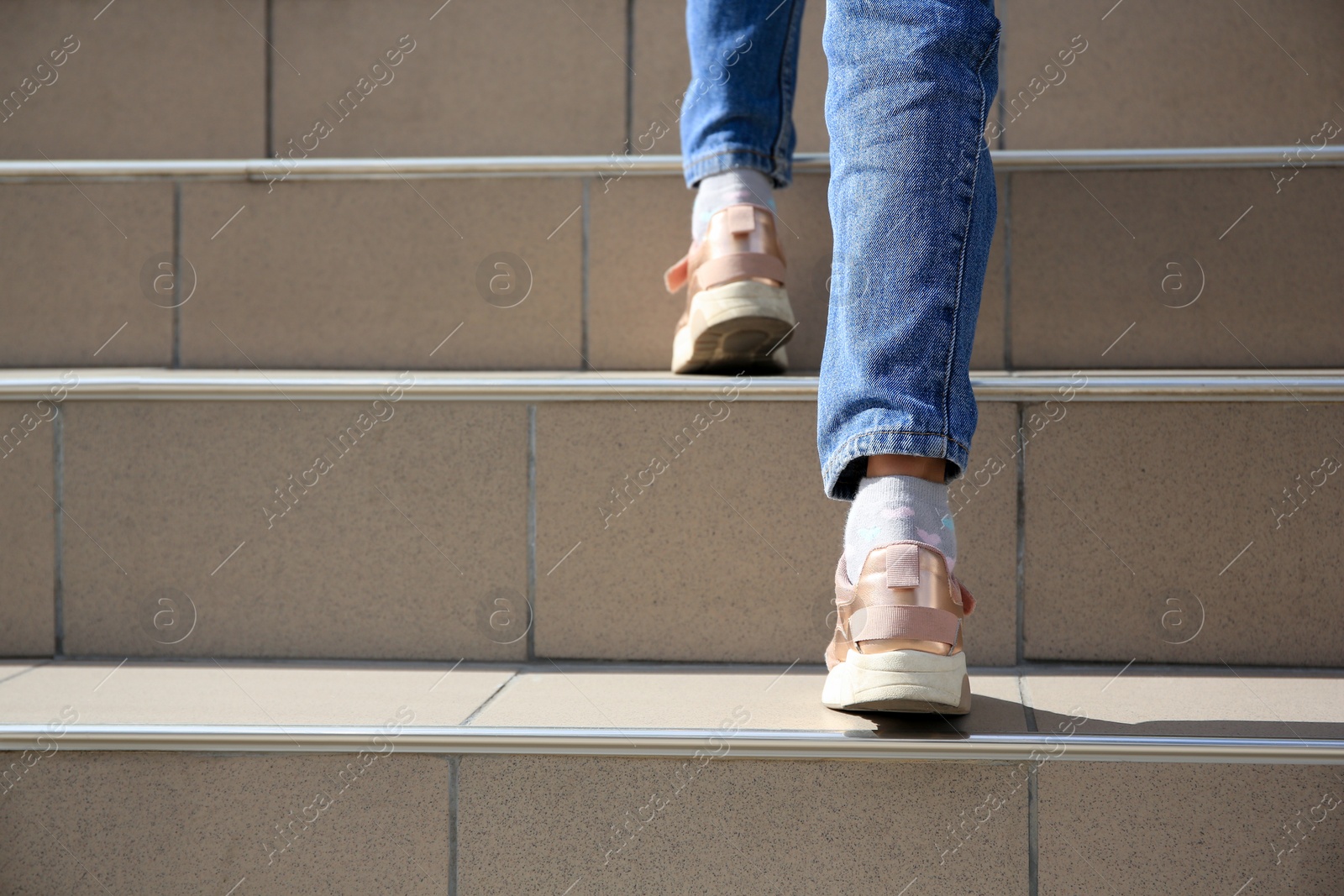 Photo of Woman walking up beige stairs outdoors, closeup