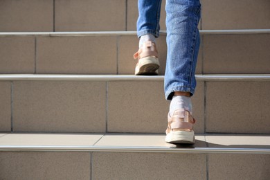 Woman walking up beige stairs outdoors, closeup