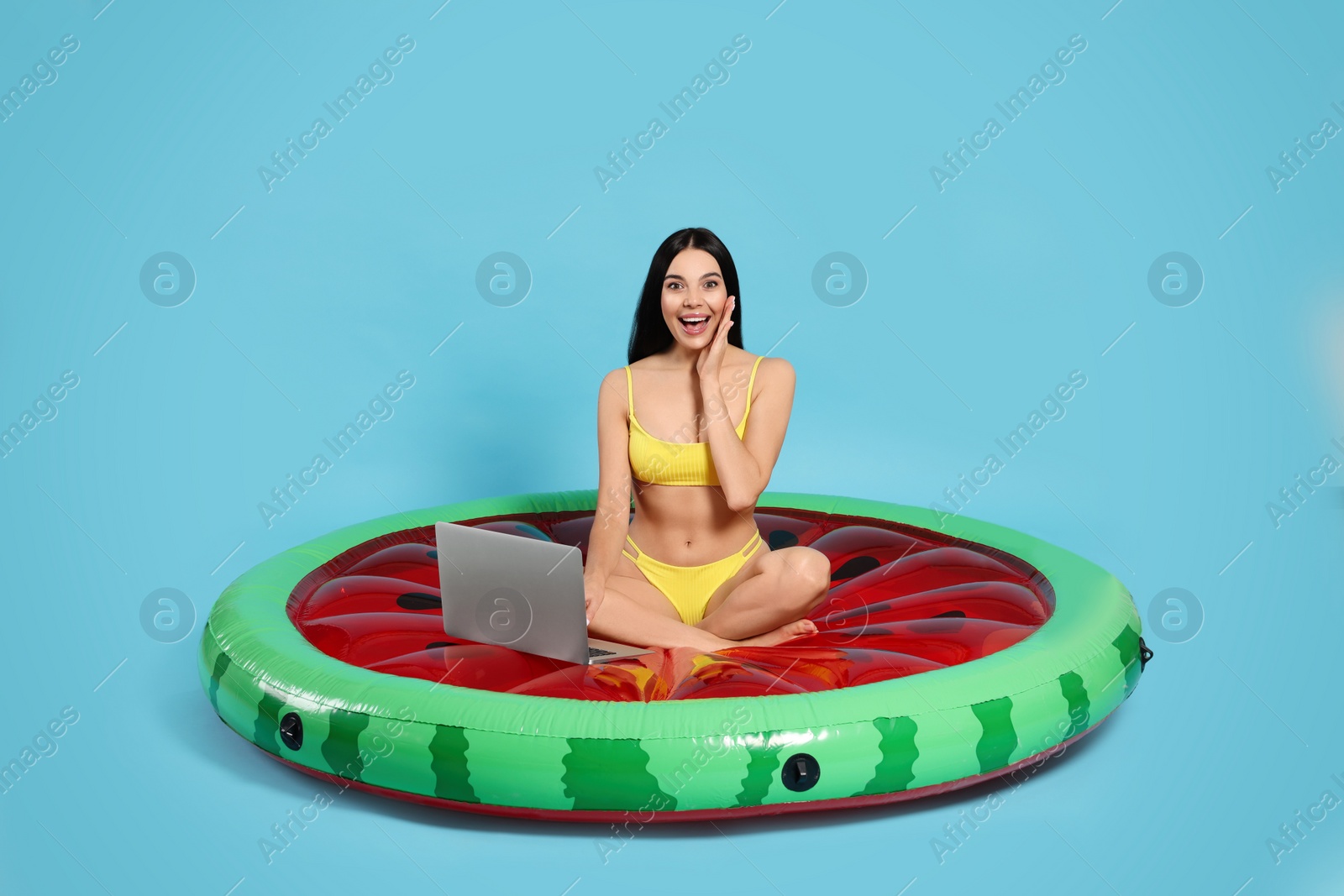 Photo of Young woman using laptop while sitting on inflatable mattress against light blue background