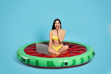 Young woman using laptop while sitting on inflatable mattress against light blue background