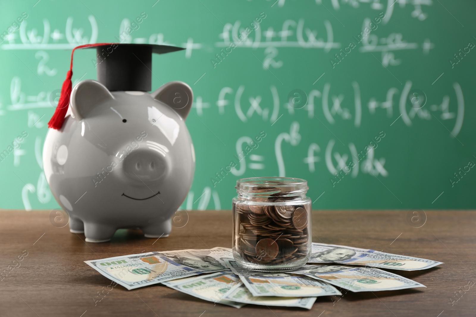 Photo of Scholarship concept. Glass jar with coins, piggy bank, graduation cap and dollar banknotes on wooden table