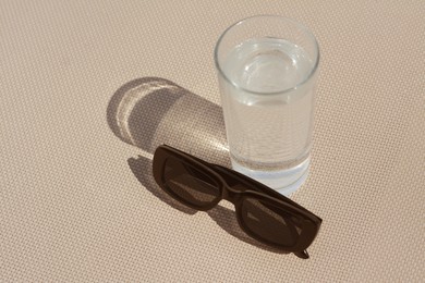 Photo of Stylish sunglasses and glass of water on grey surface, space for text