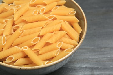 Photo of Raw penne pasta in bowl on grey table, closeup