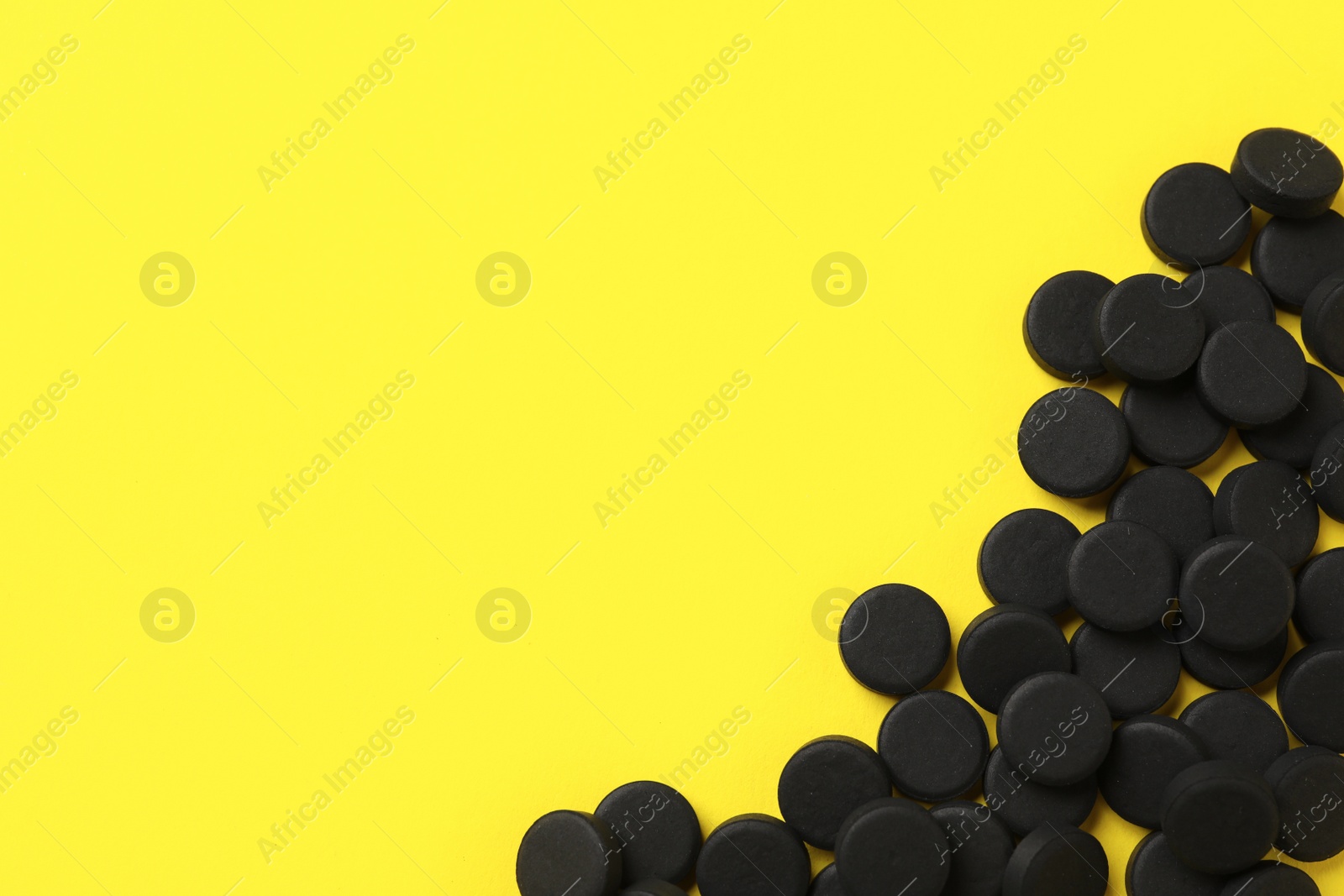 Photo of Activated charcoal pills on yellow background, flat lay with space for text. Potent sorbent