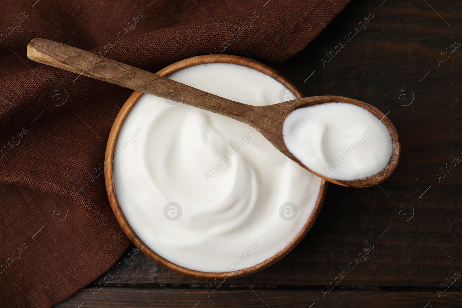 Photo of Delicious natural yogurt in bowl and spoon on wooden table, top view