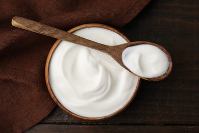 Photo of Delicious natural yogurt in bowl and spoon on wooden table, top view