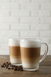 Hot coffee with milk in glass cups and beans on wooden table