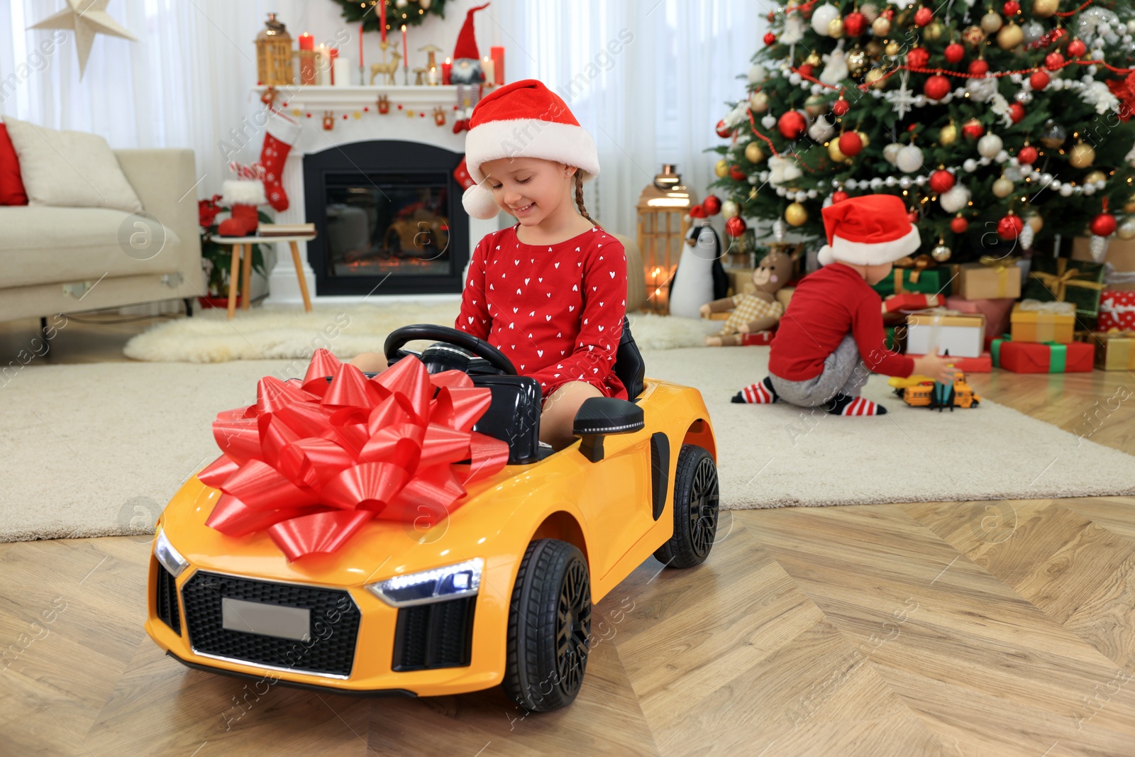 Photo of Cute little girl driving toy car in room decorated for Christmas