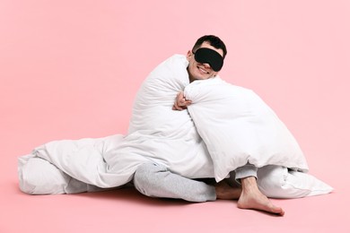 Photo of Happy man in pyjama and sleep mask wrapped in blanket on pink background
