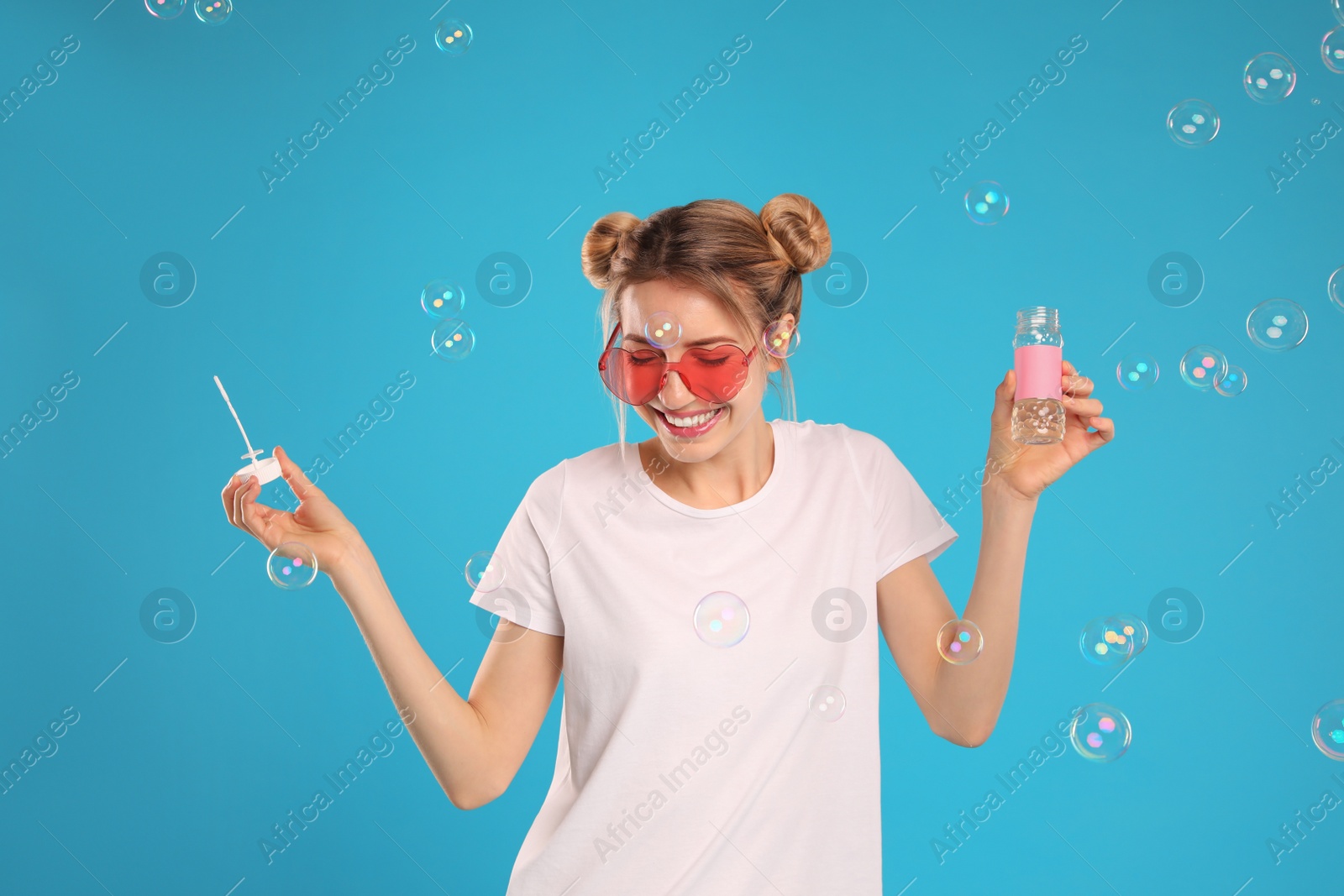 Photo of Young woman blowing soap bubbles on light blue background