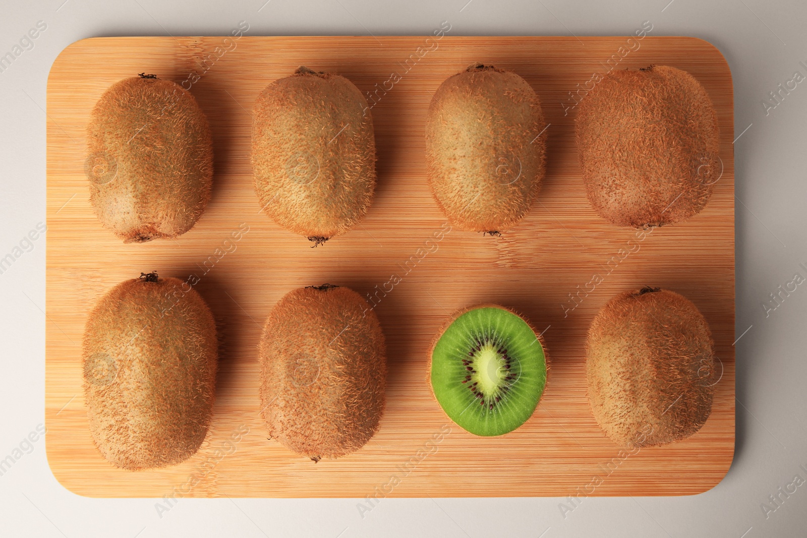 Photo of Wooden board with whole kiwis and cut one on beige background, top view
