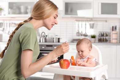 Woman feeding her child in highchair indoors. Healthy baby food