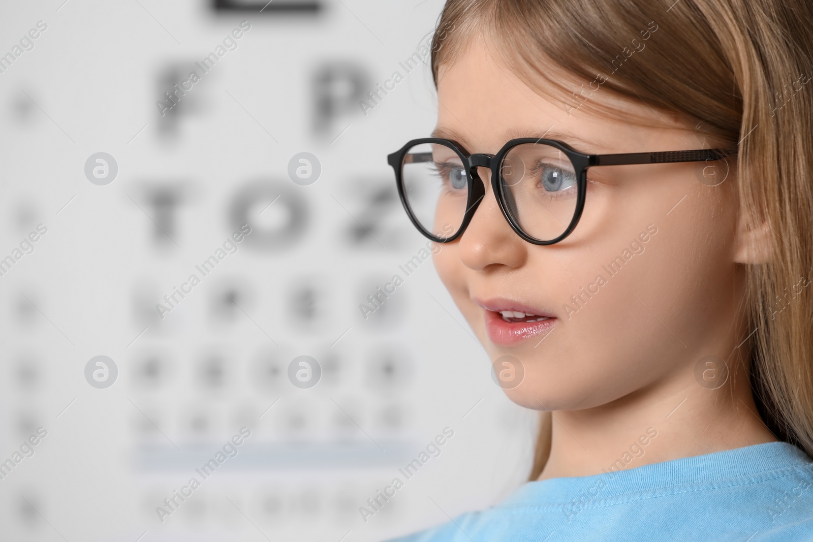 Photo of Little girl with glasses against vision test chart, closeup