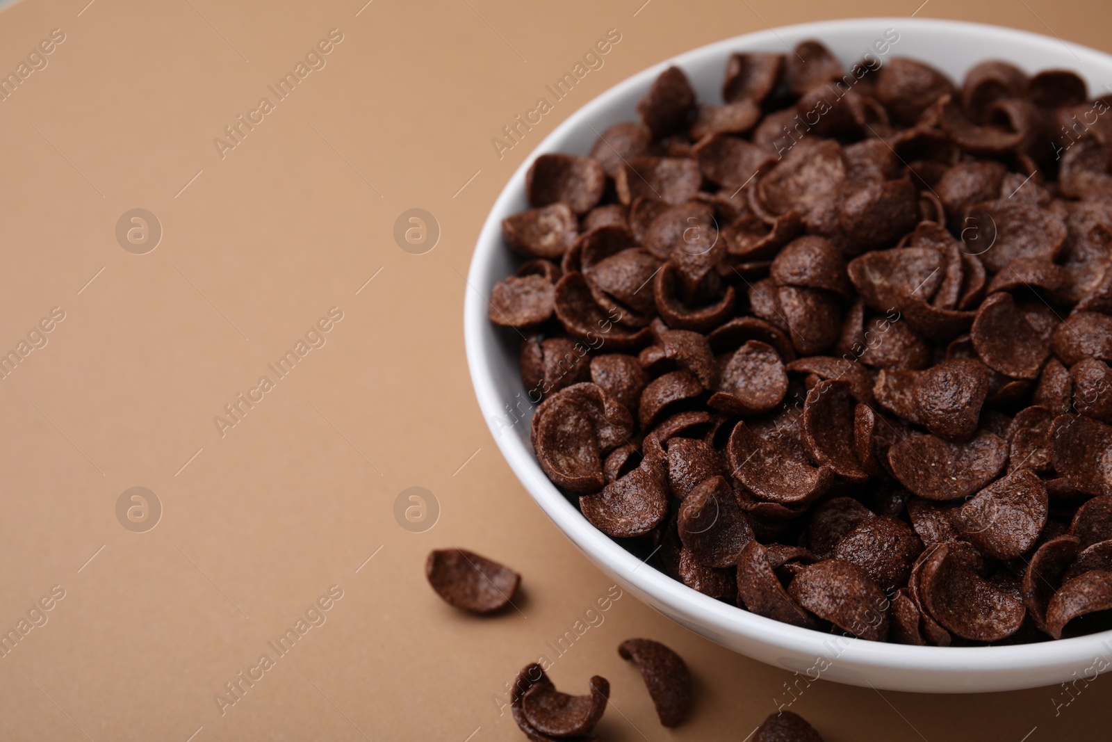 Photo of Breakfast cereal. Chocolate corn flakes in bowl on brown table, closeup. Space for text