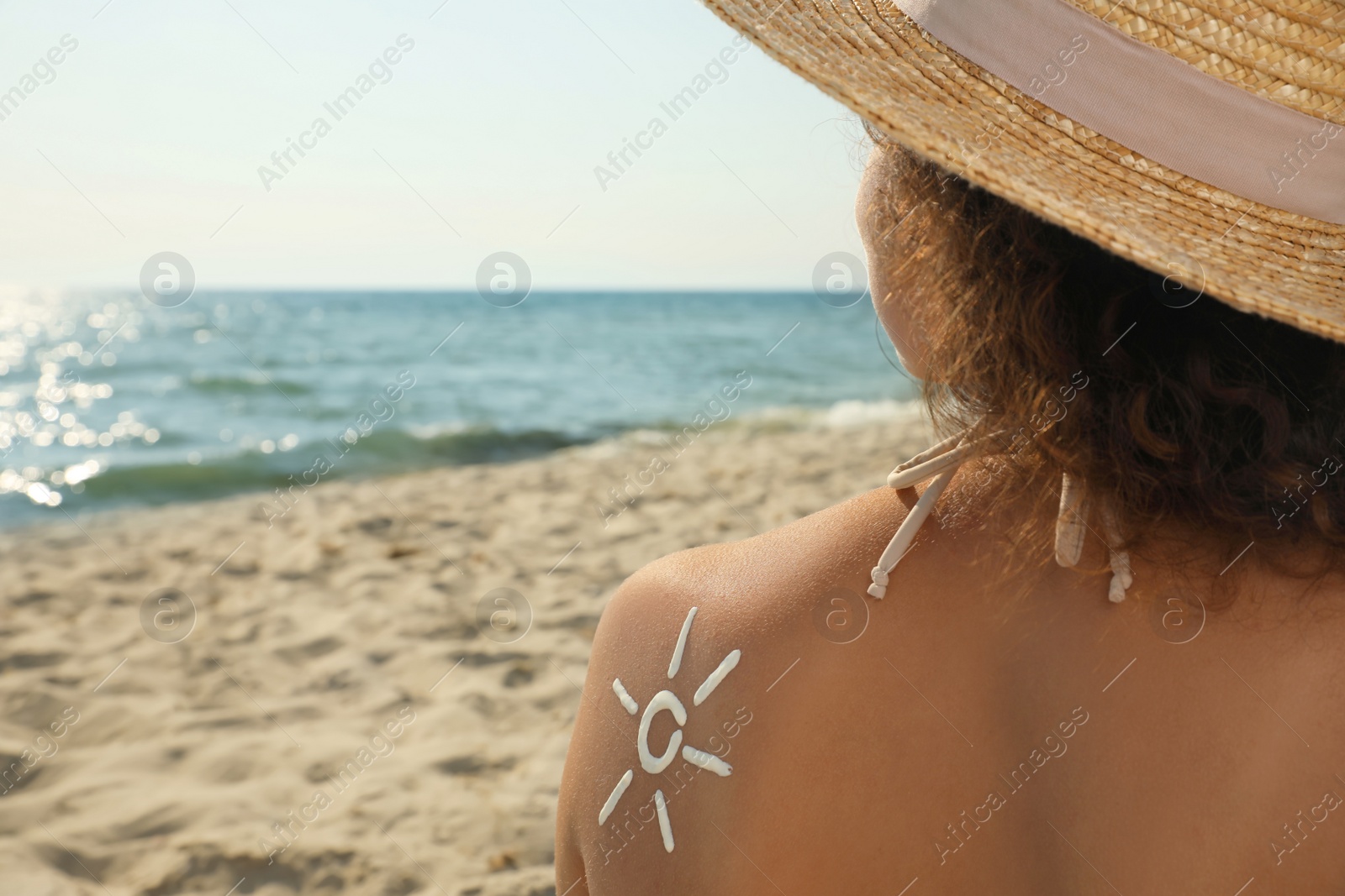 Photo of African American woman with sun protection cream on shoulder at beach, back view