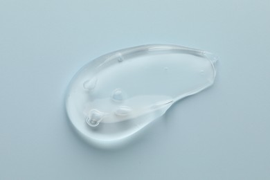 Photo of Smear of clear cosmetic gel on light blue background, top view