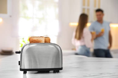 Photo of Modern toaster with slices of bread and blurred couple on background