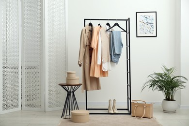 Photo of Rack with different stylish women's clothes, boots, bag and green houseplant indoors
