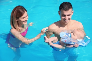 Happy parents with little baby in swimming pool on sunny day, outdoors