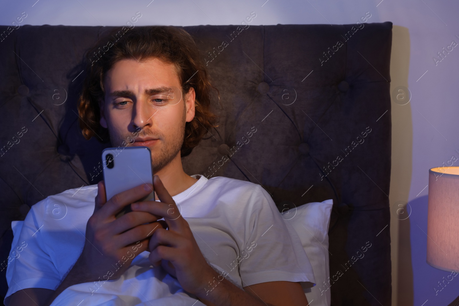 Photo of Handsome young man using smartphone in dark room at night. Bedtime