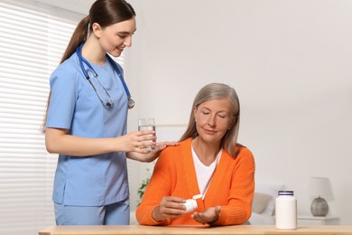 Young healthcare worker giving glass of water to senior woman indoors