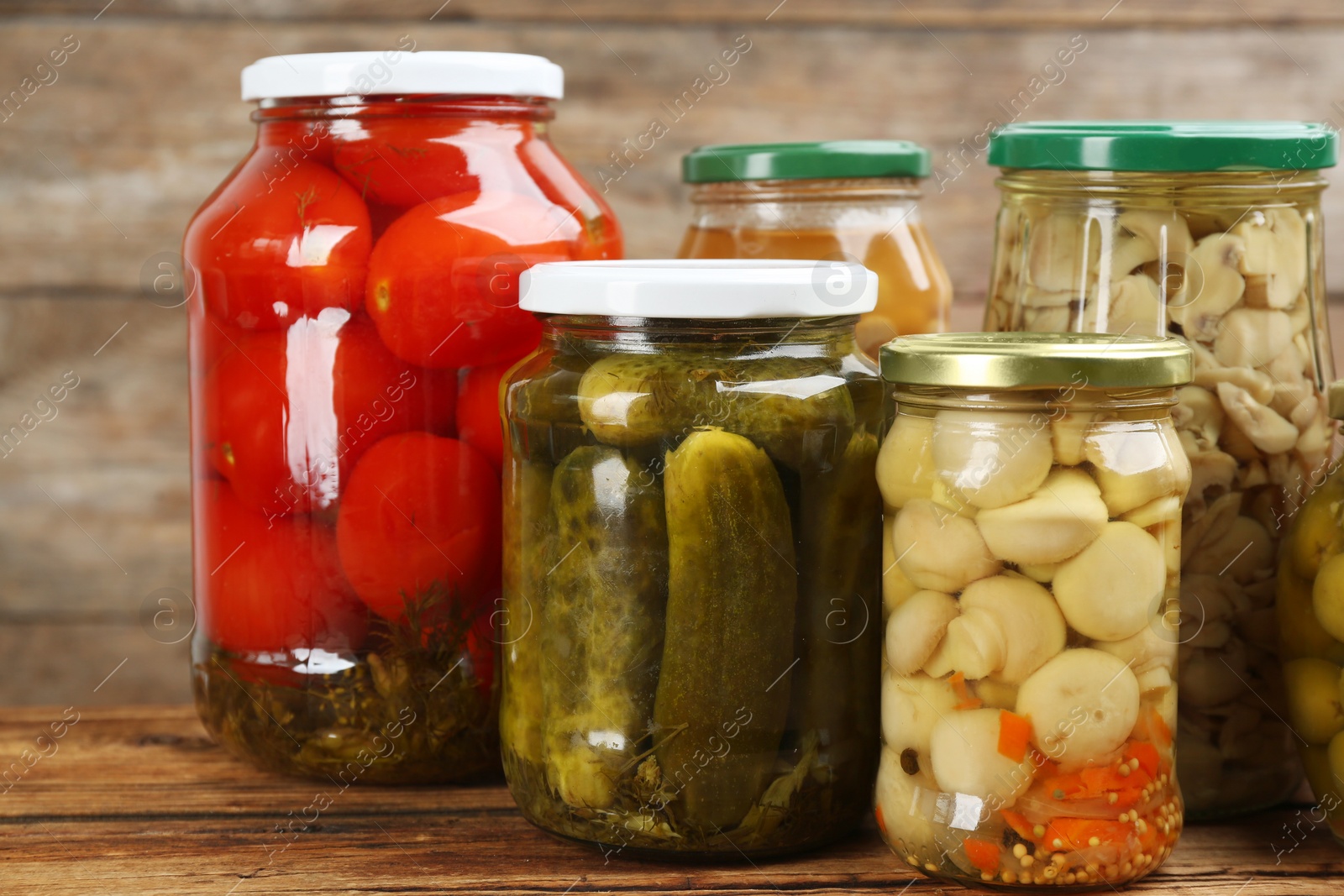 Photo of Jars of pickled vegetables on wooden table, closeup