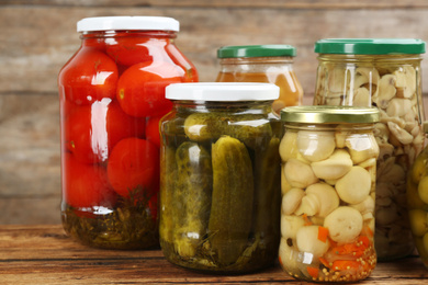 Photo of Jars of pickled vegetables on wooden table, closeup