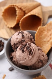 Photo of Tasty ice cream with chocolate chunks and piece of waffle cone in bowl on table, above view