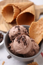 Tasty ice cream with chocolate chunks and piece of waffle cone in bowl on table, above view