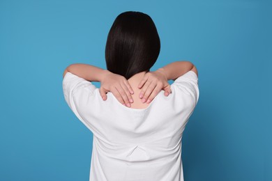 Photo of Young woman suffering from pain in neck on light blue background, back view. Arthritis symptoms