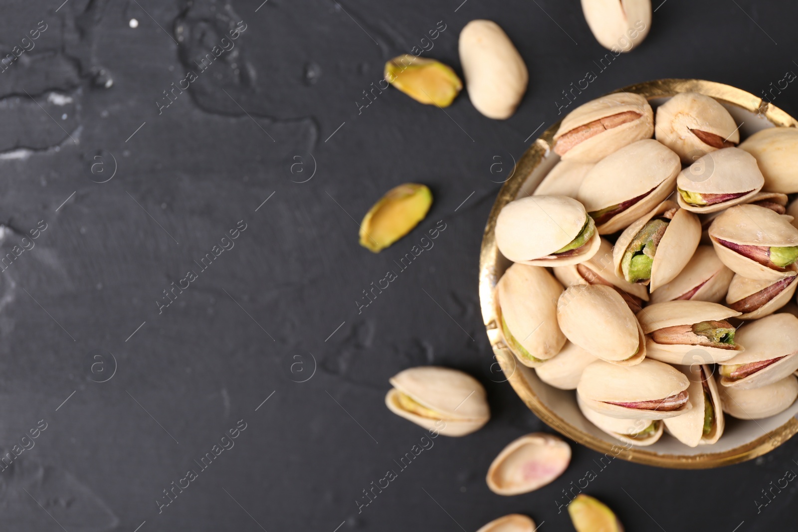 Photo of Tasty pistachios in bowl on black table, top view. Space for text