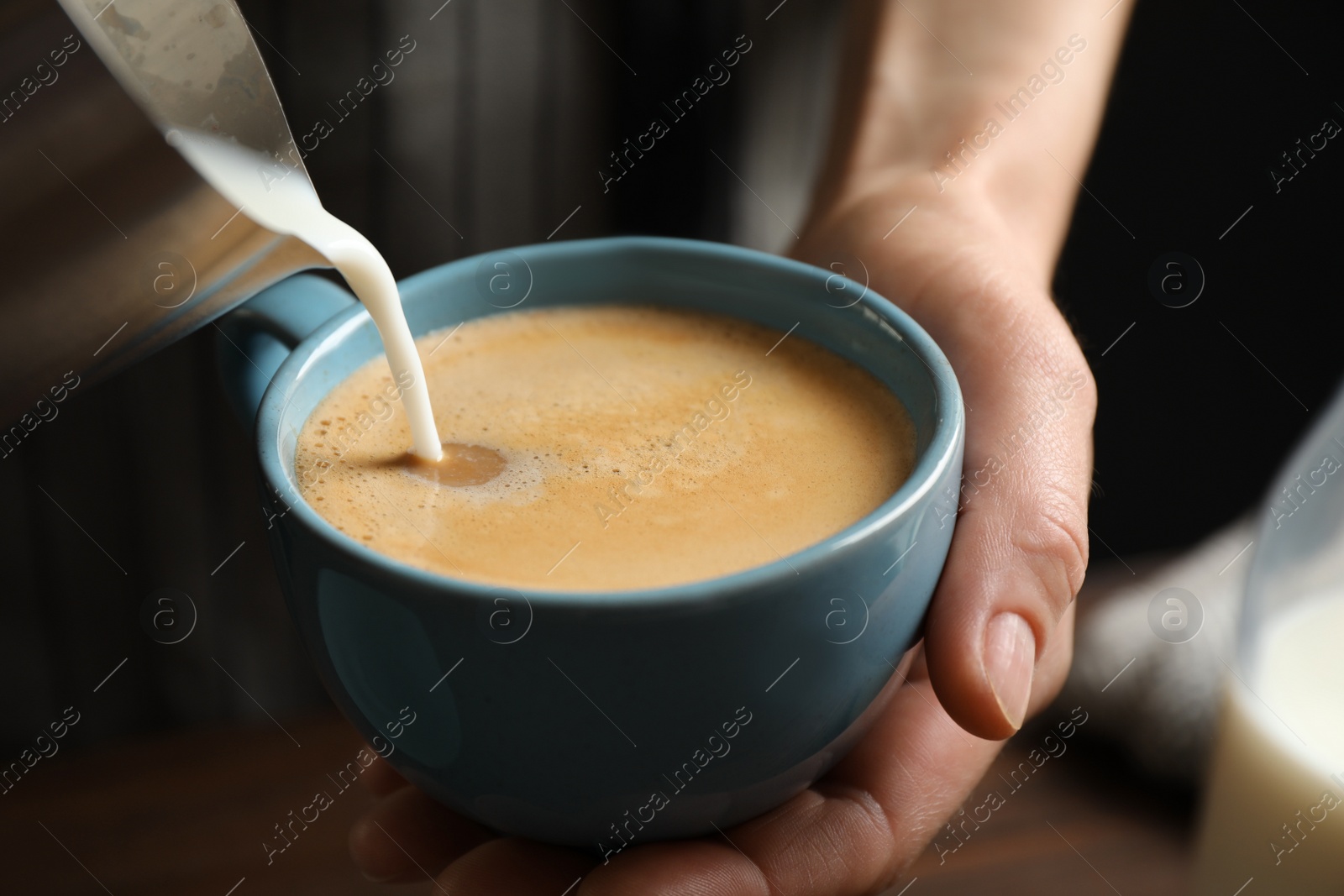 Photo of Woman pouring milk into cup of hot coffee, closeup