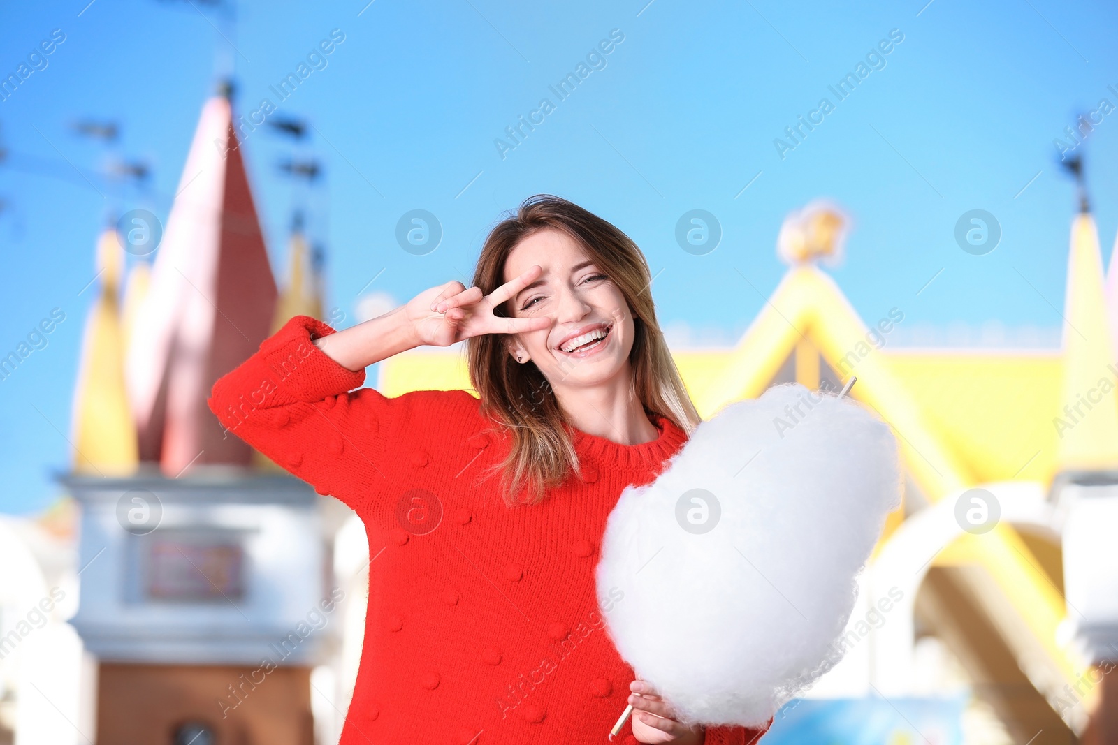 Photo of Young cheerful woman having fun with  cotton candy in amusement park