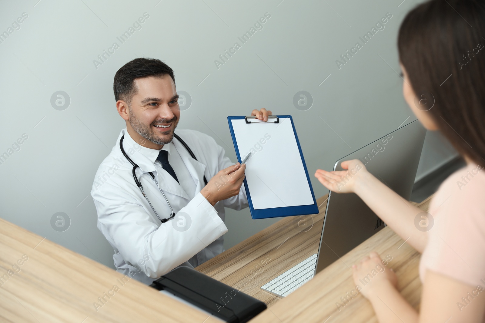 Photo of Doctor with clipboard consulting patient in clinic