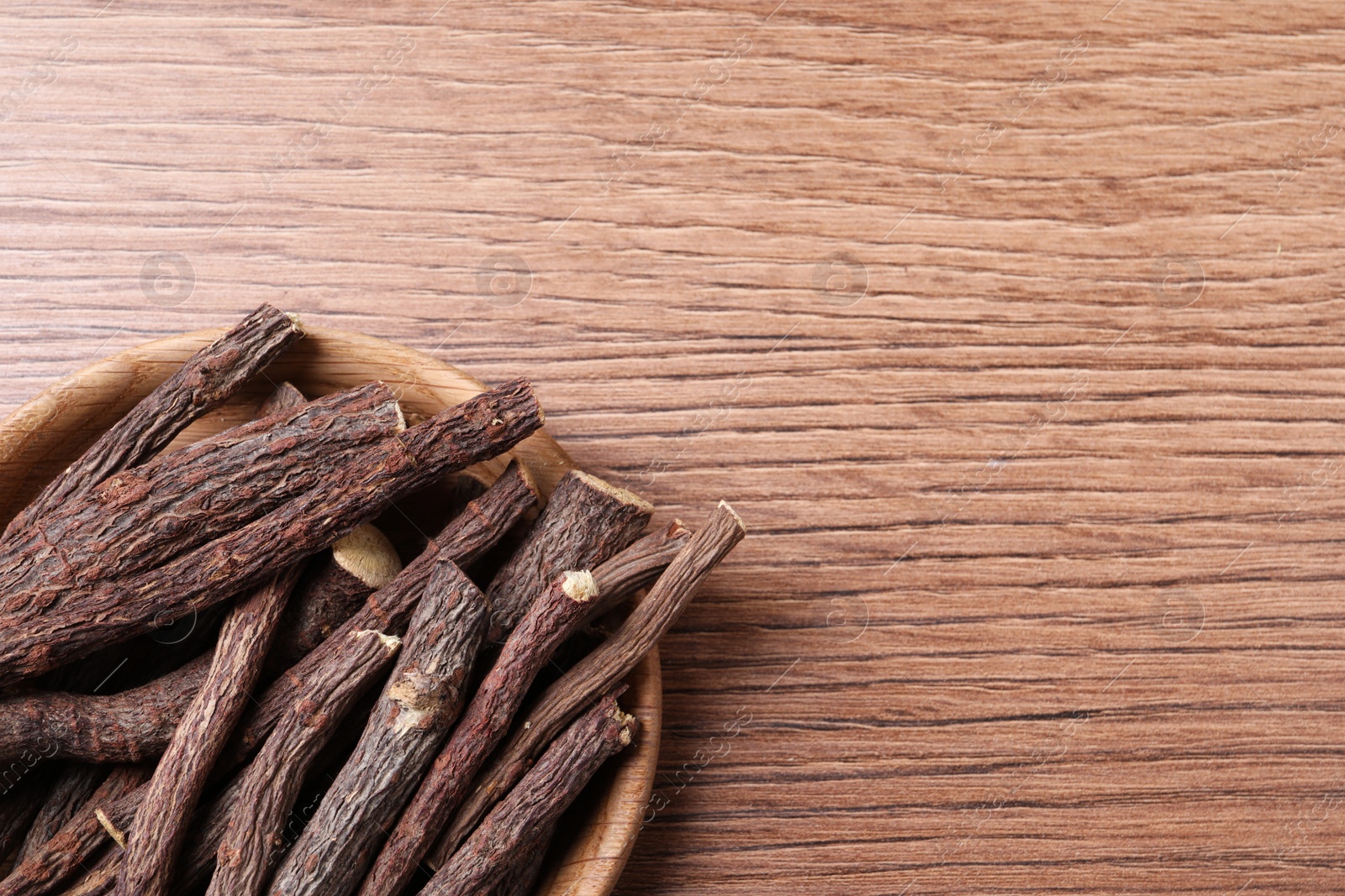 Photo of Dried sticks of liquorice root on wooden table, top view. Space for text