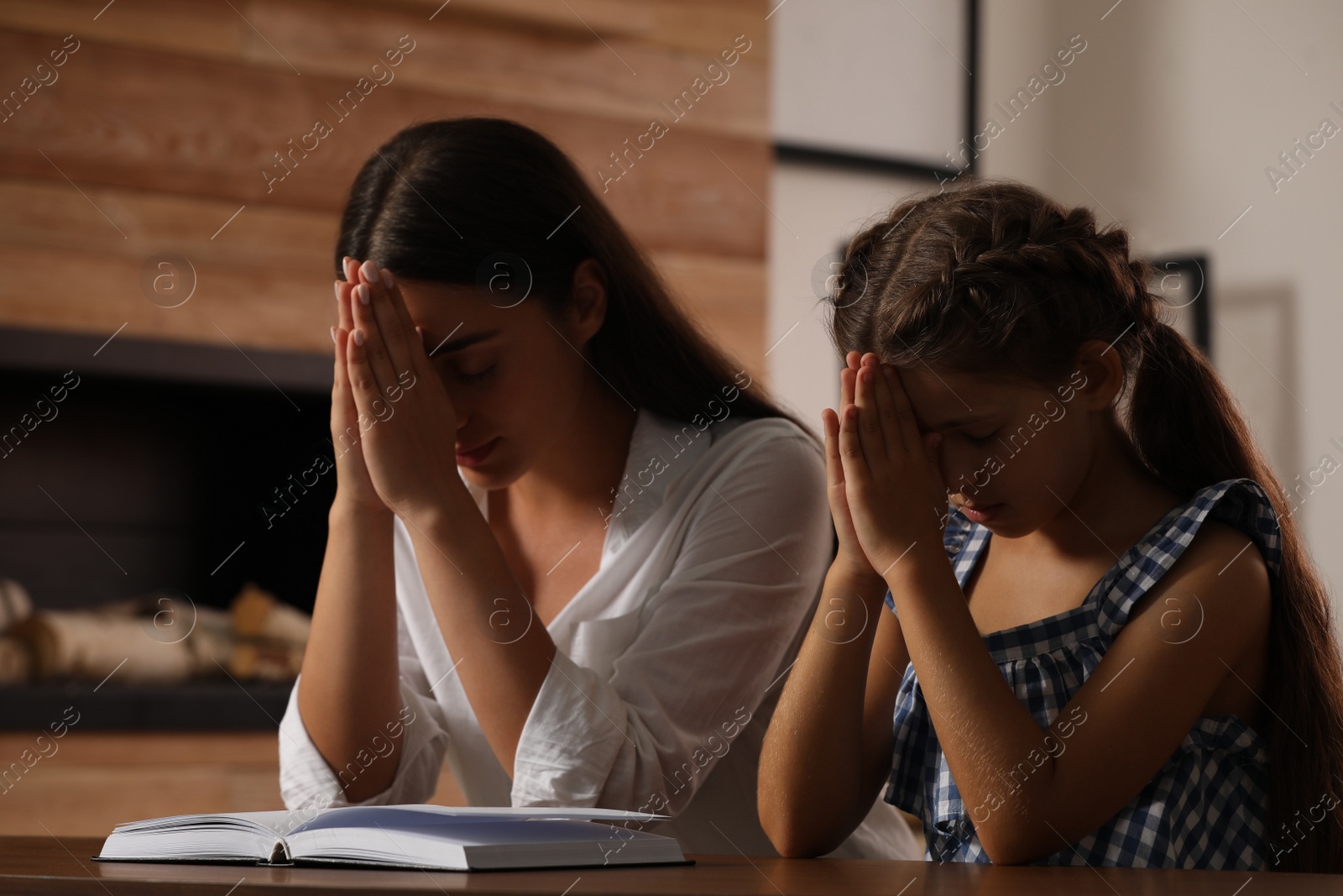 Photo of Young woman with her little daughter praying together over Bible at home