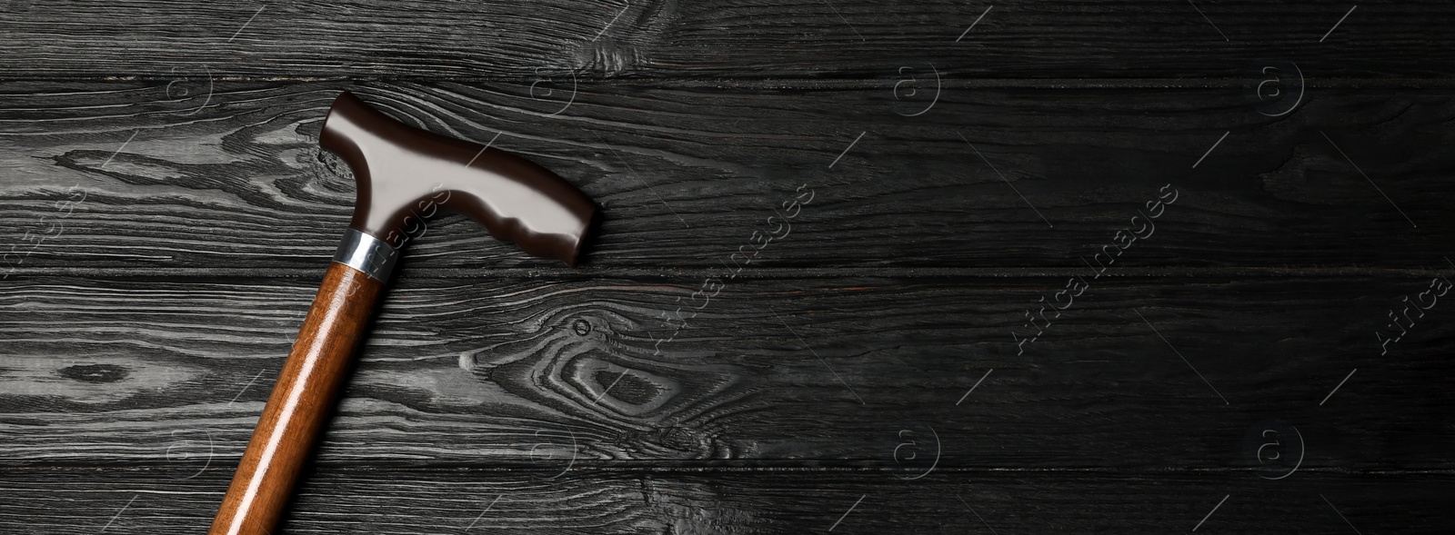 Image of Elegant walking cane on black wooden background, top view. Banner design with space for text