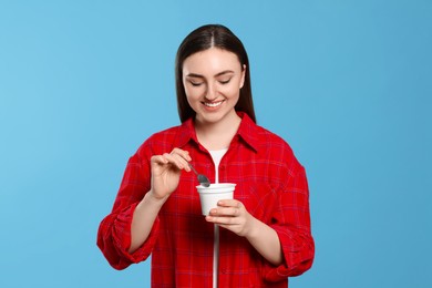 Woman with tasty yogurt on light blue background