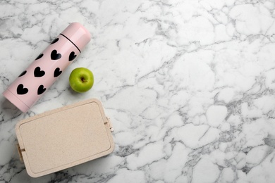 Thermos, lunch box and apple on white marble table, flat lay. Space for text