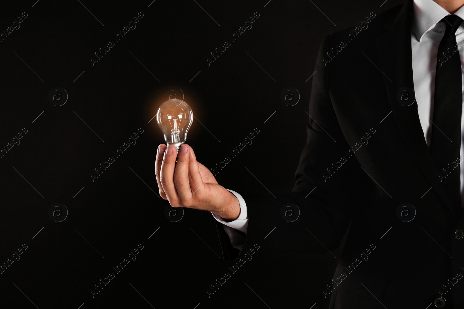 Photo of Businessman holding lamp bulb against dark background