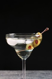 Martini cocktail with ice and olives on grey table against dark background. Space for text