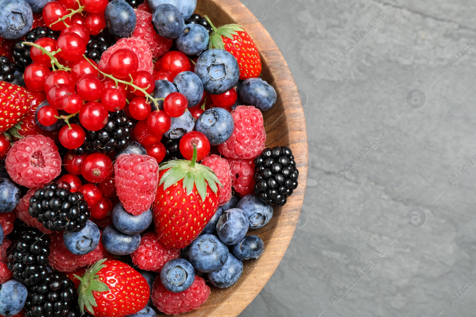 Photo of Mix of different fresh berries in bowl on grey table, top view. Space for text