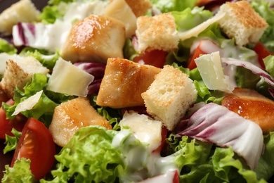 Photo of Delicious Caesar salad with fresh ingredients as background, closeup