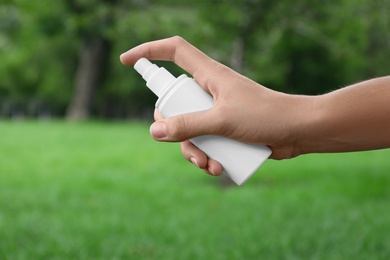 Woman with bottle of insect repellent spray outdoors, closeup