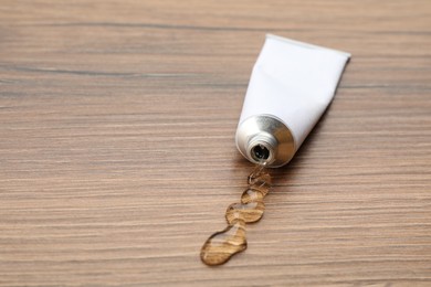 Photo of Open white tube with ointment on wooden table. Space for text