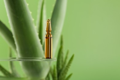 Skincare ampoule near aloe vera on light green background, closeup. Space for text