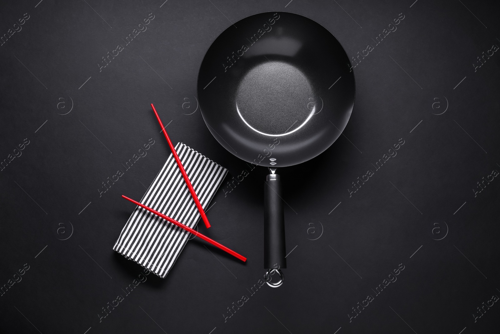 Photo of Empty iron wok and chopsticks on black table, flat lay