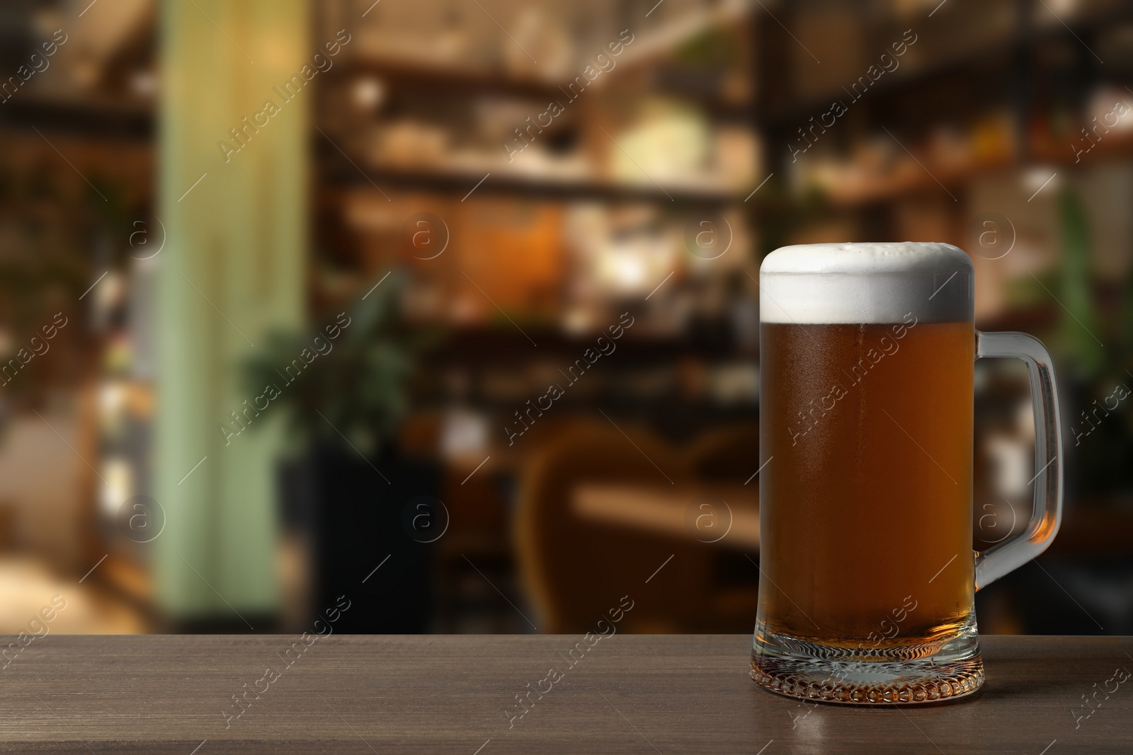 Image of Mug with fresh beer on wooden table in pub, space for text